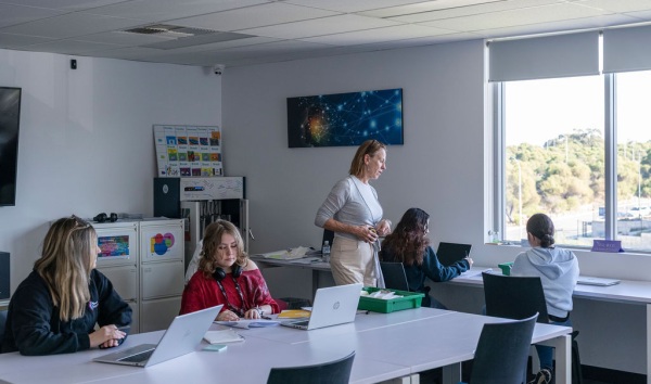 A woman walking around the room while teenage girls do their schoolwork