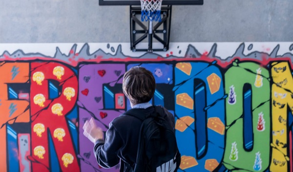 A boy taking a shot at a basketball hoop that sits above a colourful mural
