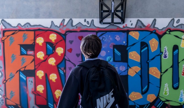 A boy shooting a basketball at a hoop that sits above a colourful mural