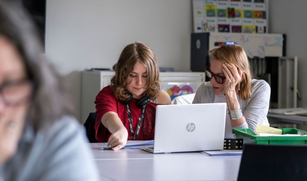 A woman sitting at a desk with a girl and explaining some schoolwork to her