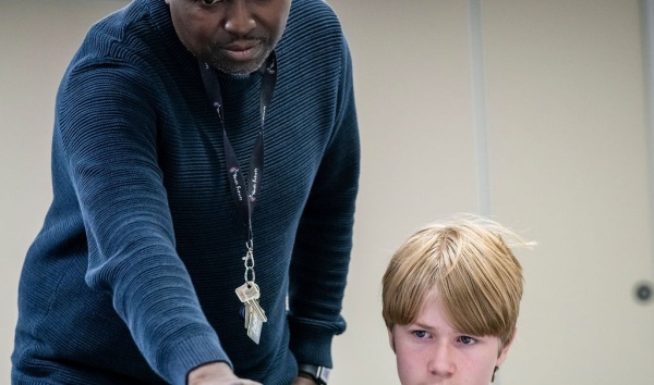 A man supervising a child working on a laptop and pointing at the screen of the laptop