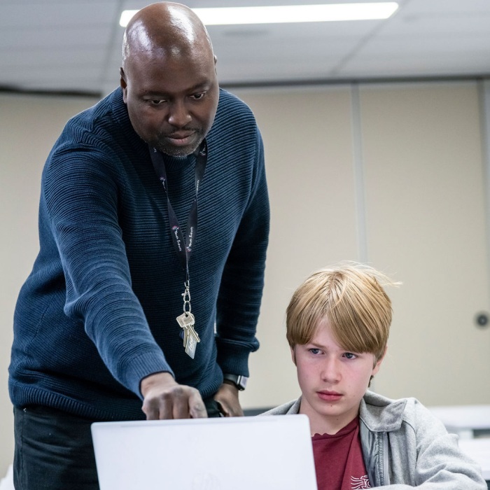 A man supervising a child working on a laptop and pointing at the screen of the laptop