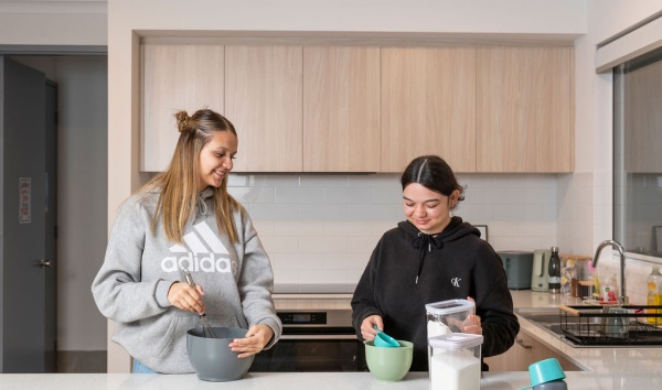 Two teenage girls standing at the kitchen counter and smiling as they measure ingredients for baking