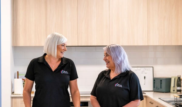 Two youth futures workers in polo shirts leaning against a kitchen counter and smiling as they chat