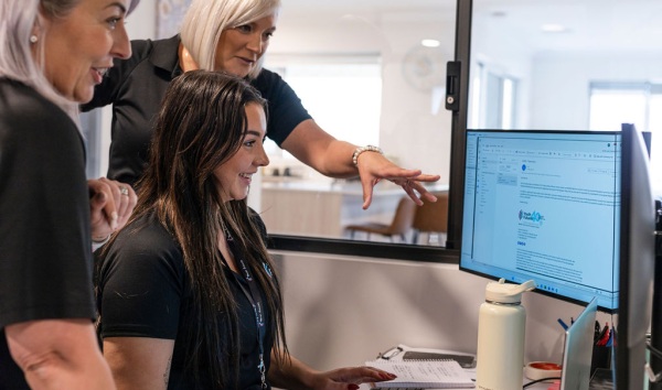 Three youth futures workers huddled around a computer smiling