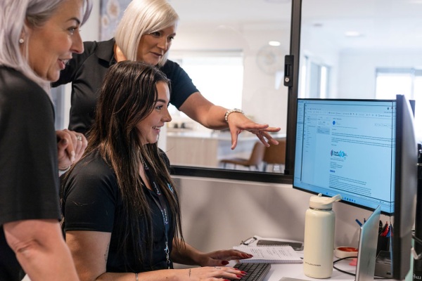 Three youth futures workers huddled around a computer smiling