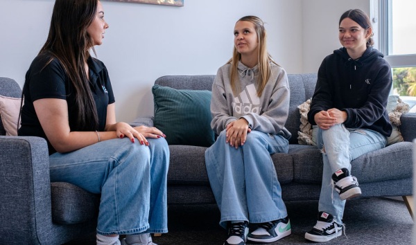 Three teenage girls sitting on couches in a living room and chatting about something