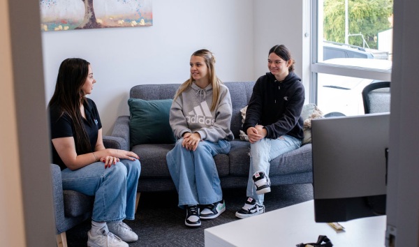 Three teenage girls sitting on couches in a living room and chatting