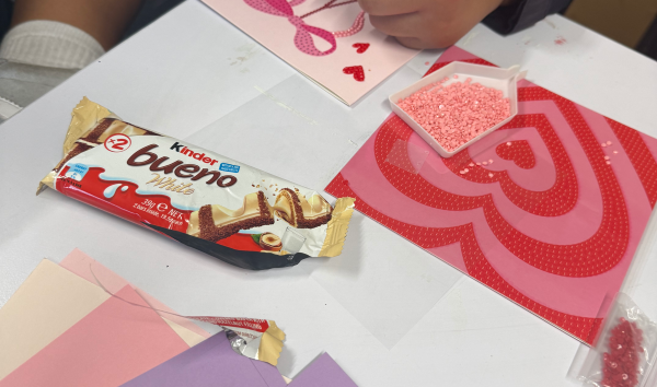 A kinder bueno chocolate bar next to some pink greeting cards that are being decorated