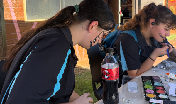 Two girls sitting at a table painting their own faces