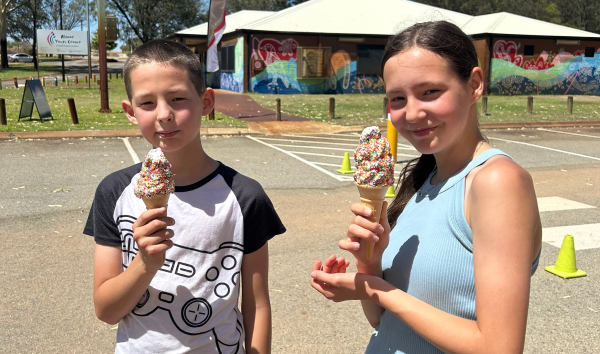 A boy and a girl eating soft serve ice creams with sprinkles in a parking lot