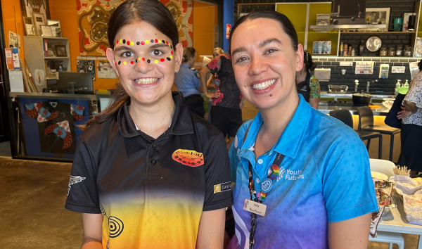 A youth futures volunteer and a child that has black, yellow and red face paint both smiling