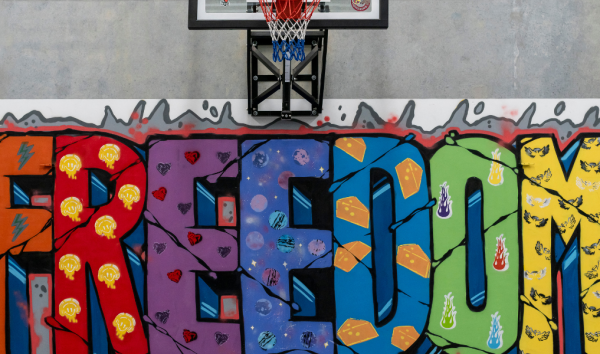 Street mural that says the word freedom in different colours and patterns below a basketball hoop
