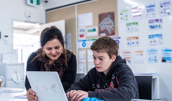 A woman sitting next to a boy and looking at this laptop with him