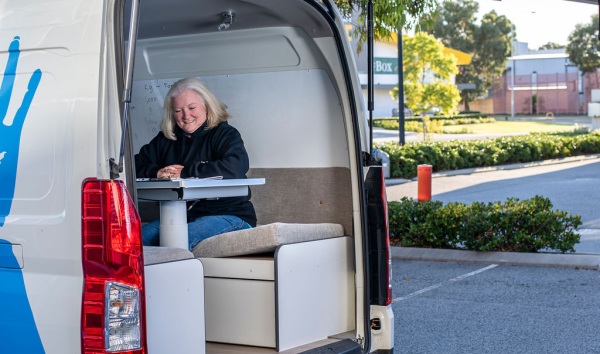 A van with an open boot and a woman sitting at a desk inside the van