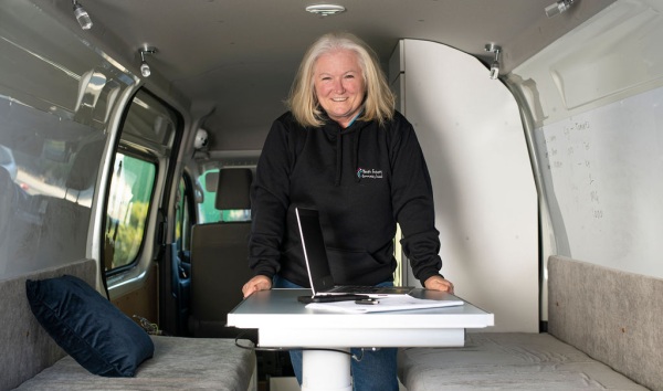 A woman smiling at the camera while she leans on a desk inside a van