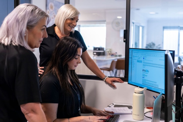 Two women standing behind another woman while she does some work on a computer