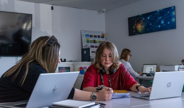 A woman sitting at a table with a teenage student and explaining some schoolwork by pointing at the worksheet
